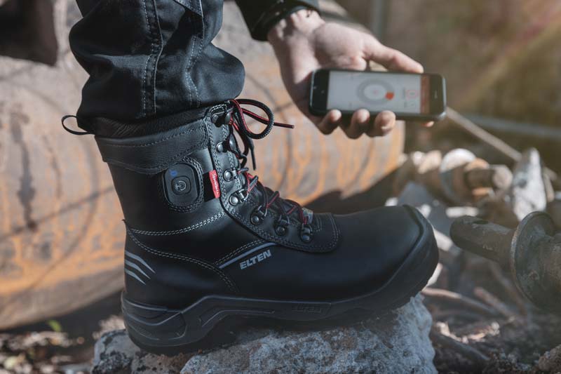 Beheizbarer ELTEN Johnny Sicherheitsstiefel und ein Handy mit zugehöriger App.